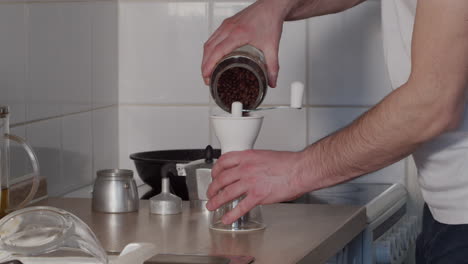 Man-prepares-coffee-beans-for-grinder,-turns-crank-to-grind