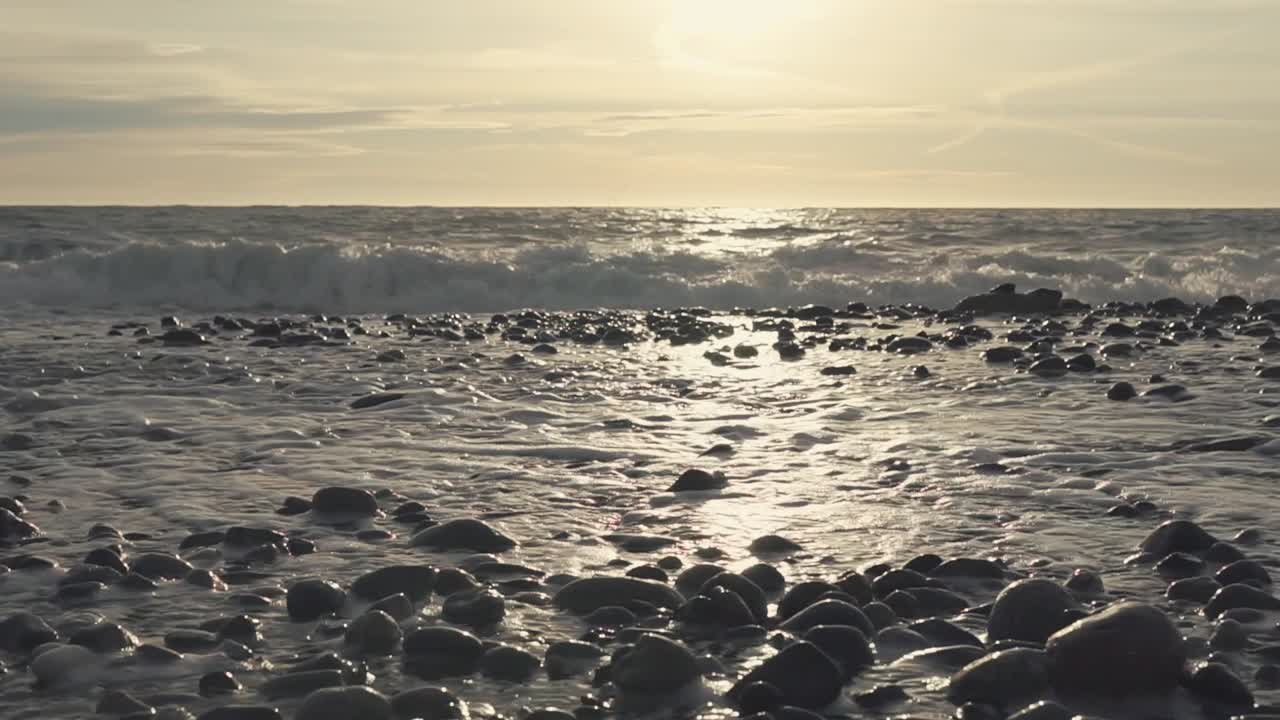 바위 해변의 해가 지고 파도가 불고 있습니다.