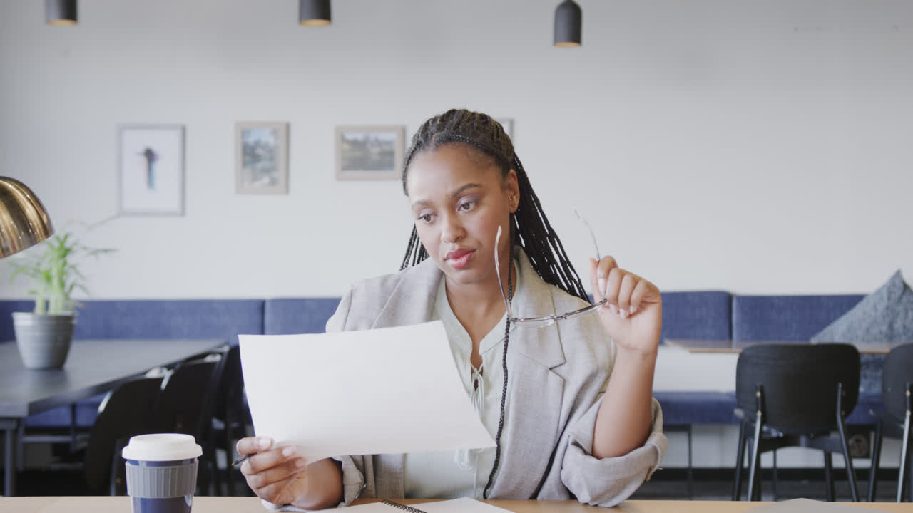 Seria donna d'affari afroamericana in abiti casual che guarda documenti durante una videochiamata, al rallentatore