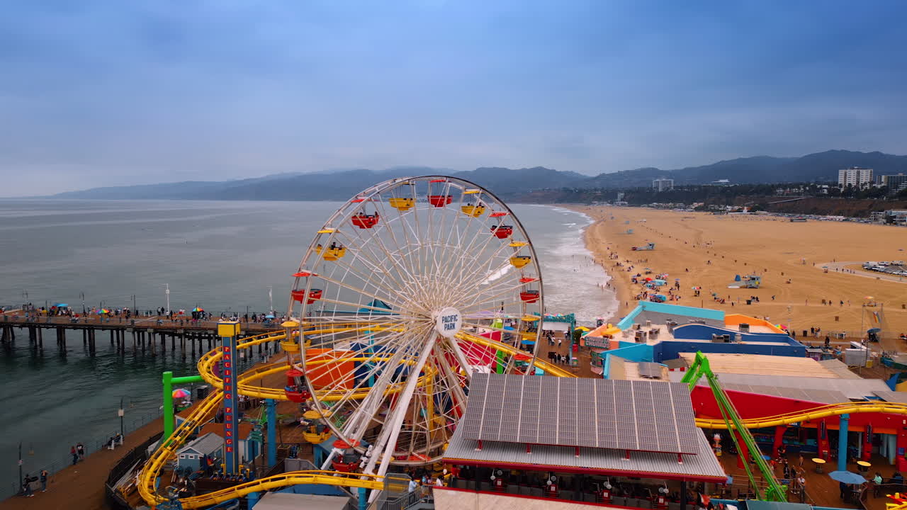 Los Angeles, USA, 29 August 2025: Approaching working Ferris Wheel at the Amusement Pacific Park in Santa Monica, LA, California, USA. Ocean, sandy beach and mountain range at backdrop