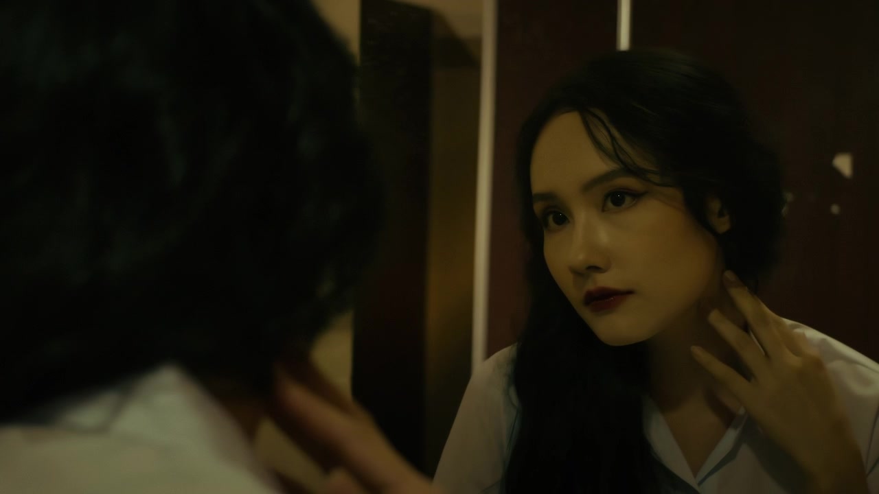 Donna asiatica con lunghi capelli scuri e rossetto che si guarda allo specchio.