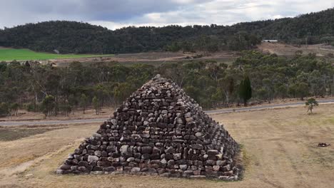 drone camera steadily approaches a large granite stone pyramid in a dry, grassy landscape near stanthorpe, queensland, under overcast daylight