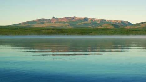 peaceful shot of alumine lake in neuquen province, argentina. the clear blue water stretches out beneath distant andes mountains, reflecting the sky and surrounded by natural patagonian forest
