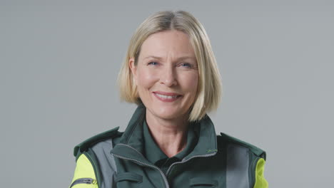 studio portrait of smiling mature female paramedic against plain background