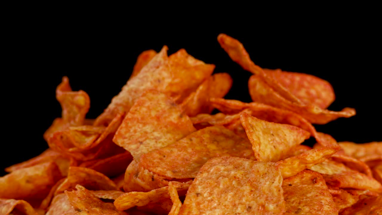 Le tortilla chips dorate ai nachos ruotano sotto le luci dello studio, rivelando la consistenza croccante e i dettagli del condimento