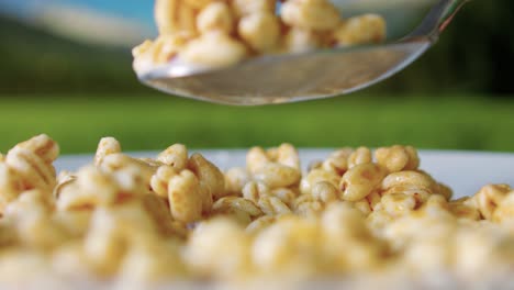 Extreme-close-up-eating-cereals-from-a-bowl-with-a-spoon-with-soy-milk-scooping-in-slow-motion-on-a-sunny-day-with-mountains-background