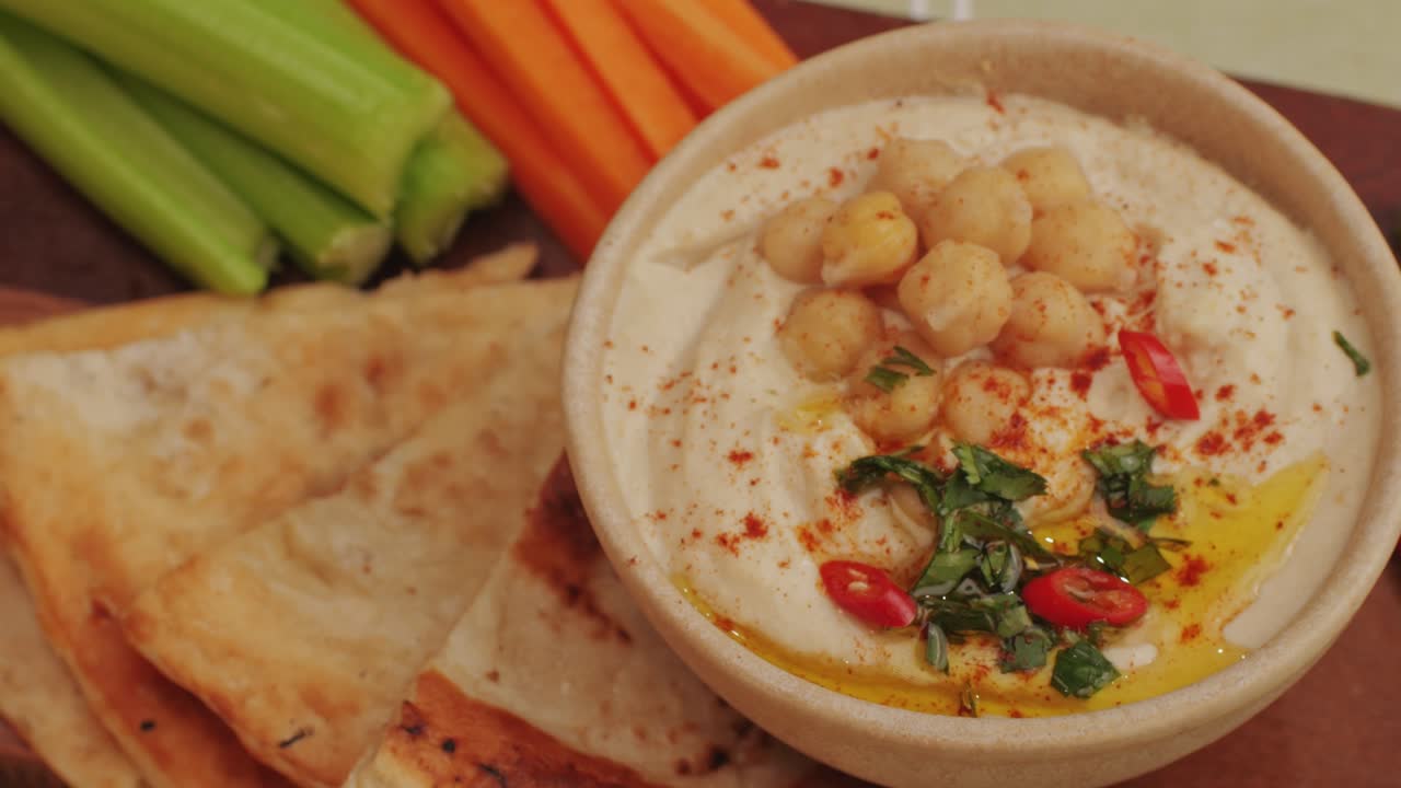 Hummus among fresh vegetables on table close-up. Hummus garnished with chickpeas, olive oil, spices and greens. Hummus or fava, a hearty snack of legumes. Kosher healthy vegan food. Lean, vegetarian dish