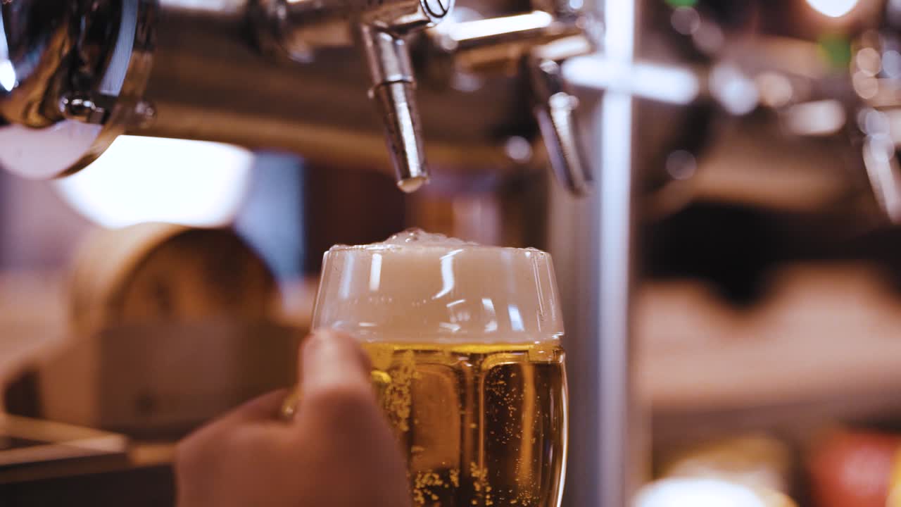 Bartender filling up with a blonde craft beer into a pint glass (slow motion)