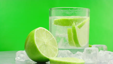 slow motion product video of a refreshing gin tonic, alcoholic summer drink with green lemons and ice blocks, isolated on a green background