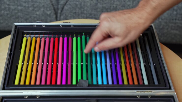 Closeup of a hand picking a green pencil from neatly arranged colorful pencils in a case. Symbolizes creativity, education, choice, and artistic work