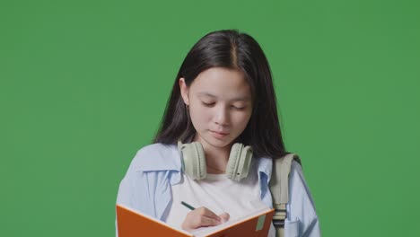 close up of asian teen girl student taking note on notebook and celebrating while standing in the green screen background studio