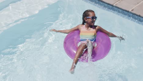 Feliz-Chica-Afroamericana-Sentada-En-Un-Anillo-De-Natación-En-La-Piscina,-Cámara-Lenta