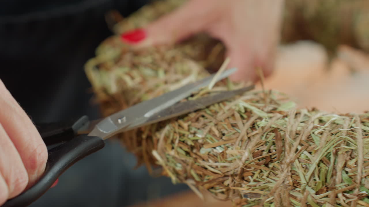 Closeup of woman cutting straw wreath with scissors, focusing on detailed crafting process, handmade decoration, rustic style, and precision in floral design preparation using natural dried plant material