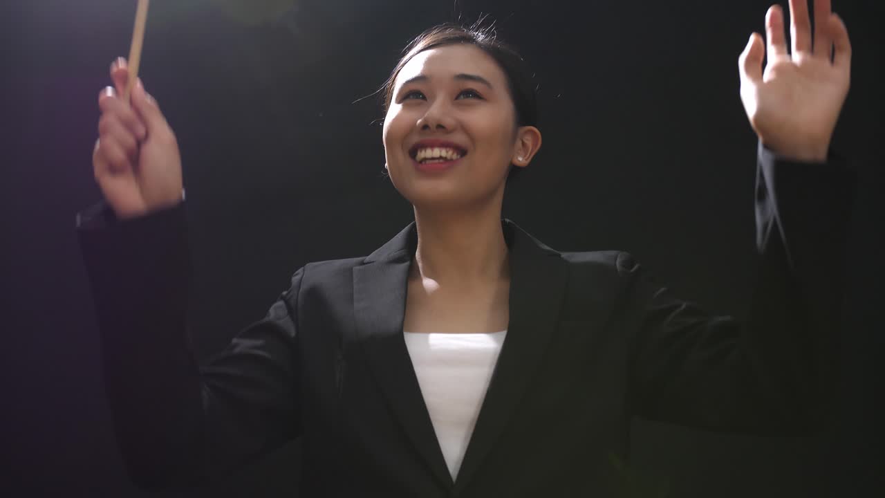 mujer conductor asiática sosteniendo un bastón y mostrando un gesto rápidamente en el estudio negro con niebla