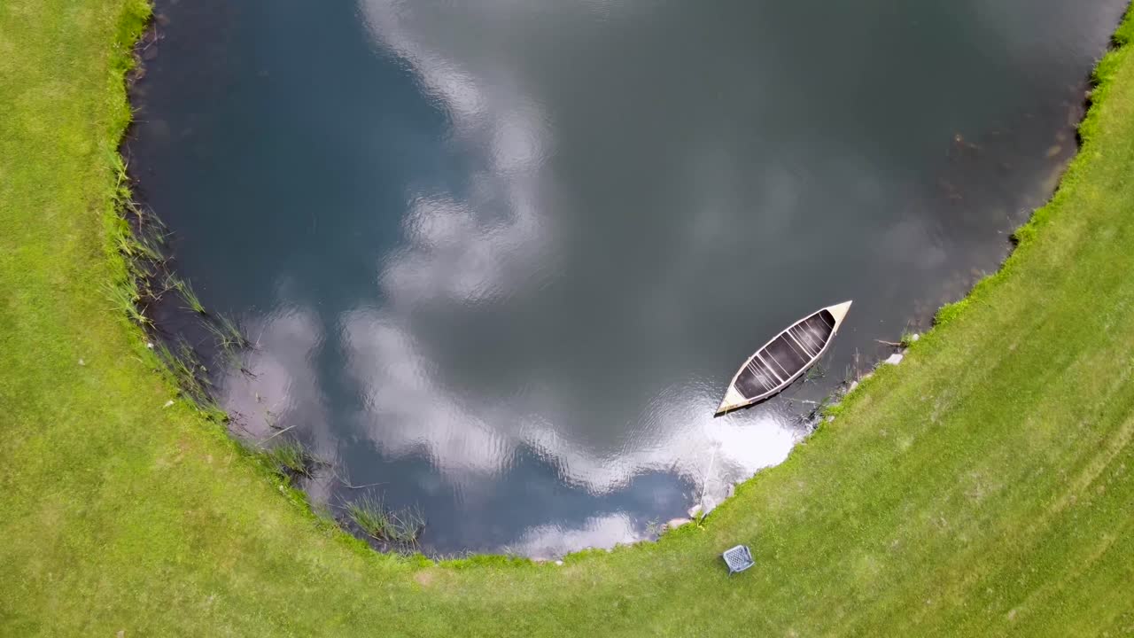 canoa vacía flotando en un estanque con nubes reflejadas en el agua