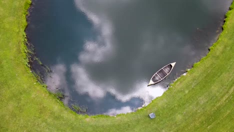 Leeres-Kanu-Schwimmt-In-Einem-Teich-Mit-Wolken,-Die-Sich-Im-Wasser-Spiegeln