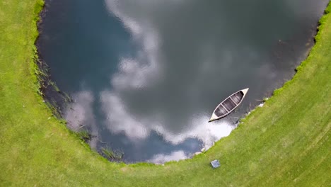 Canoa-Vacía-Flotando-En-Un-Estanque-Con-Nubes-Reflejadas-En-El-Agua