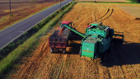 a combine harvester unloads grains into a farm truck during harvest - drone shot