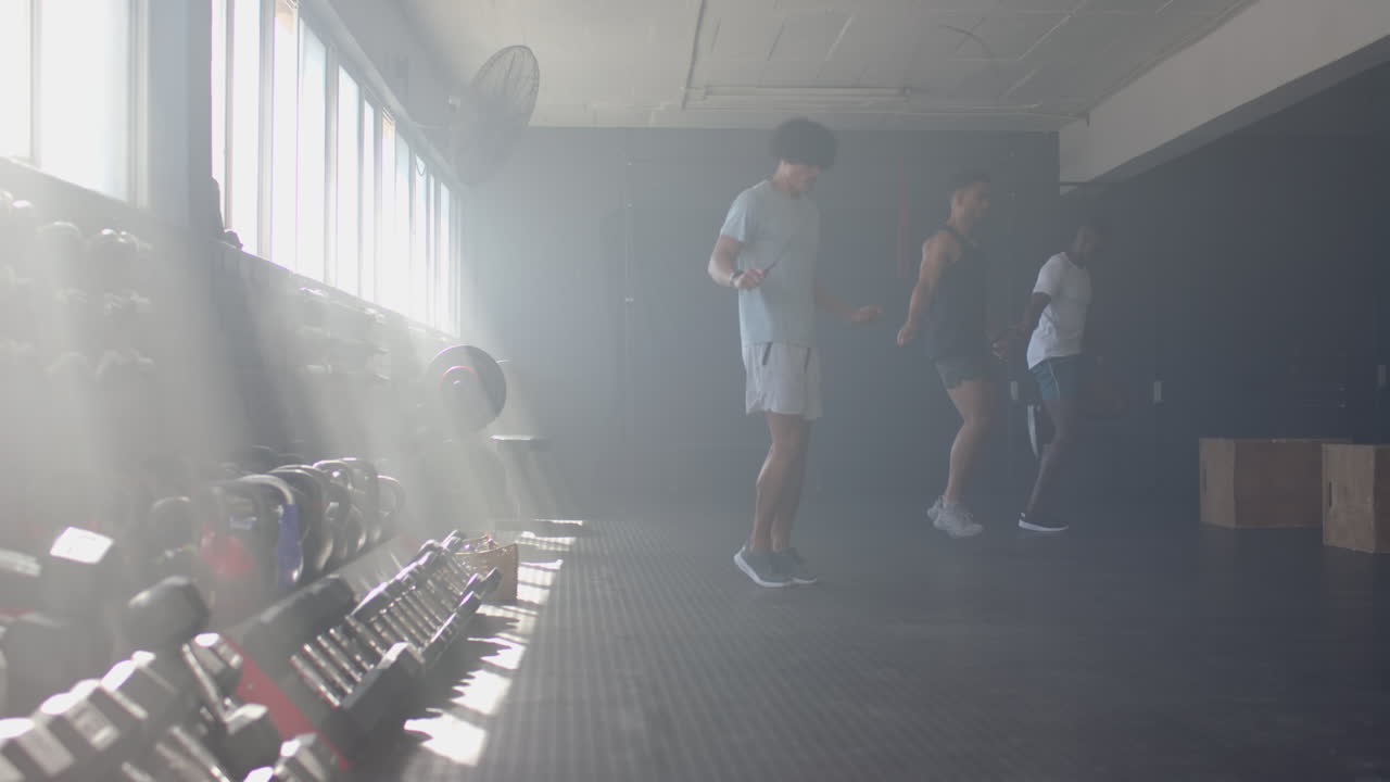 Jumping rope, three men exercising together in gym with weights in background