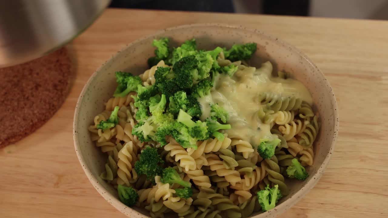 Salsa cremosa mista versata su pasta con broccoli in una ciotola di legno sul tavolo.