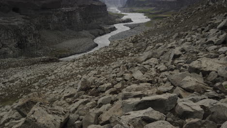 Smooth-tilt-up-reveal-of-the-Jökulsá-á-Fjöllum-river-carving-its-way-through-the-glacial-landscapes-of-Iceland-below-the-Dettifoss-Waterfall,-second-most-powerful-in-Europe