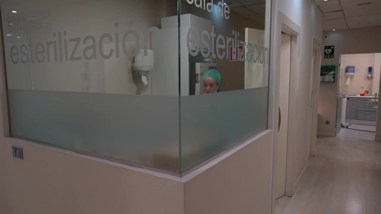 Higienista dental trabalha na sala de esterilização dentro de uma clínica moderna, com panorâmica para o corredor.
