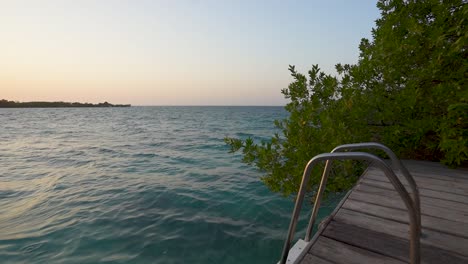 a picturesque scene of a ladder on a dock extending into the ocean, against stunning sunset over ocean waves