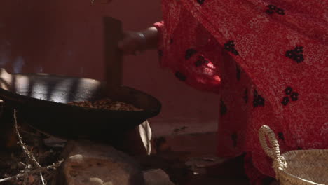 old woman placing argan seeds in pan to cook them by fire