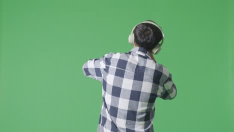 back view of young asian teen boy holding a microphone and rapping on the the green screen background