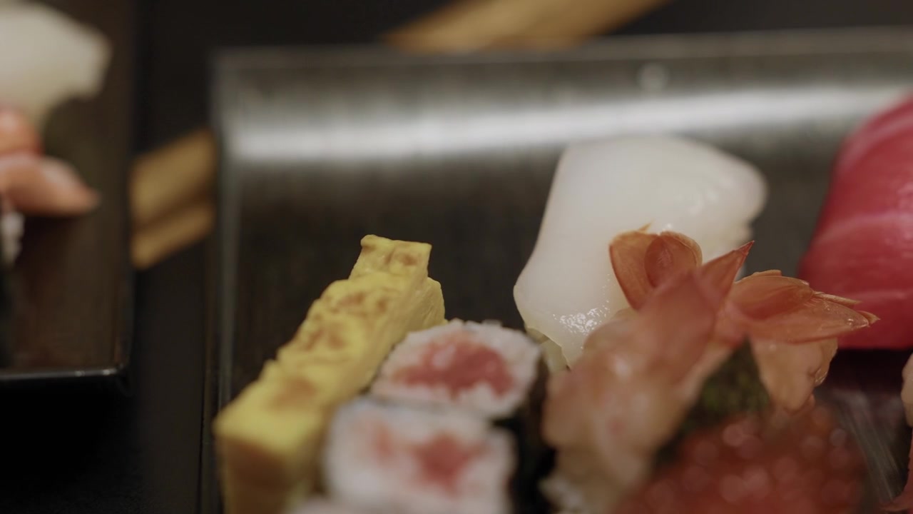 箸で卵焼き寿司を掴む、イカとマグロの隣で。日本。