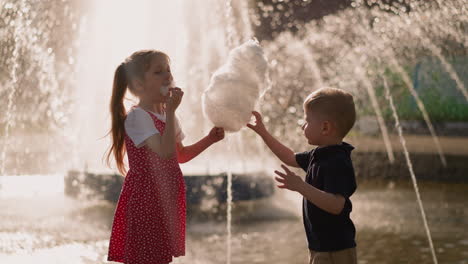 Kleines-Mädchen-Mit-Bruder-Isst-Zuckerwatte-In-Der-Nähe-Des-Brunnens