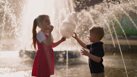 una niña con un hermano come algodón de azúcar cerca de la fuente