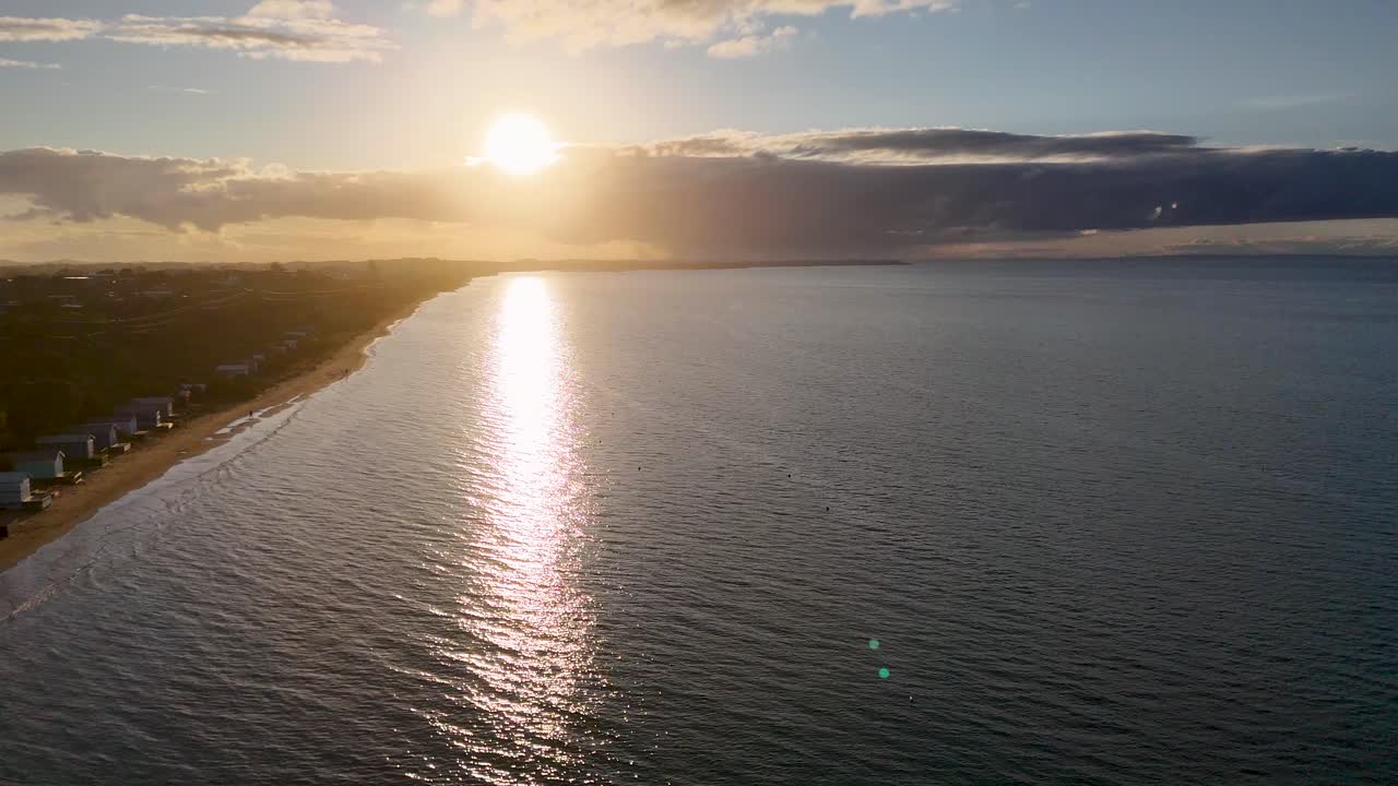 Aerial view of sunset reflecting on sea, sandy beach, and colorful bathing boxes