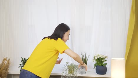 집에서 꽃에 물을 주는 젊은 여성. 그는 행복하고 즐기고 있습니다.