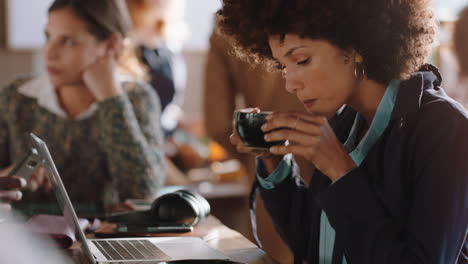 Junge-Frau-Mit-Gemischter-Abstammung-Benutzt-Laptop-Und-Arbeitet-Im-Café,-Tippt-E-Mails,-Teilt-Nachrichten-In-Sozialen-Medien-Und-Trinkt-Gerne-Kaffee,-Während-Sie-In-Einem-Belebten-Restaurant-Arbeitet