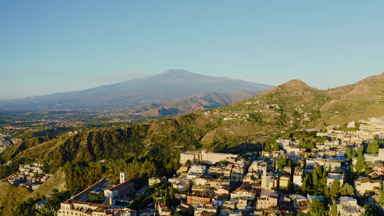 Letecký pohled na italské město v horách s výhledem na nejaktivnější sopku Evropy. Město Taormina s horou Etna v pozadí.