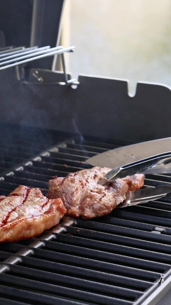 Beef steaks cooking on a grill with tongs flipping them. Outdoor ...