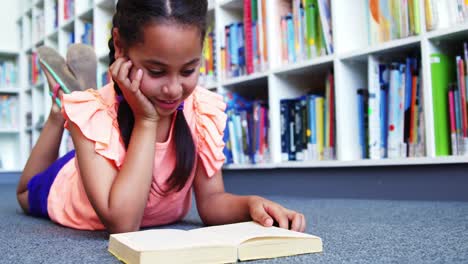 escolar acostada en el suelo y leyendo un libro en la biblioteca de la escuela