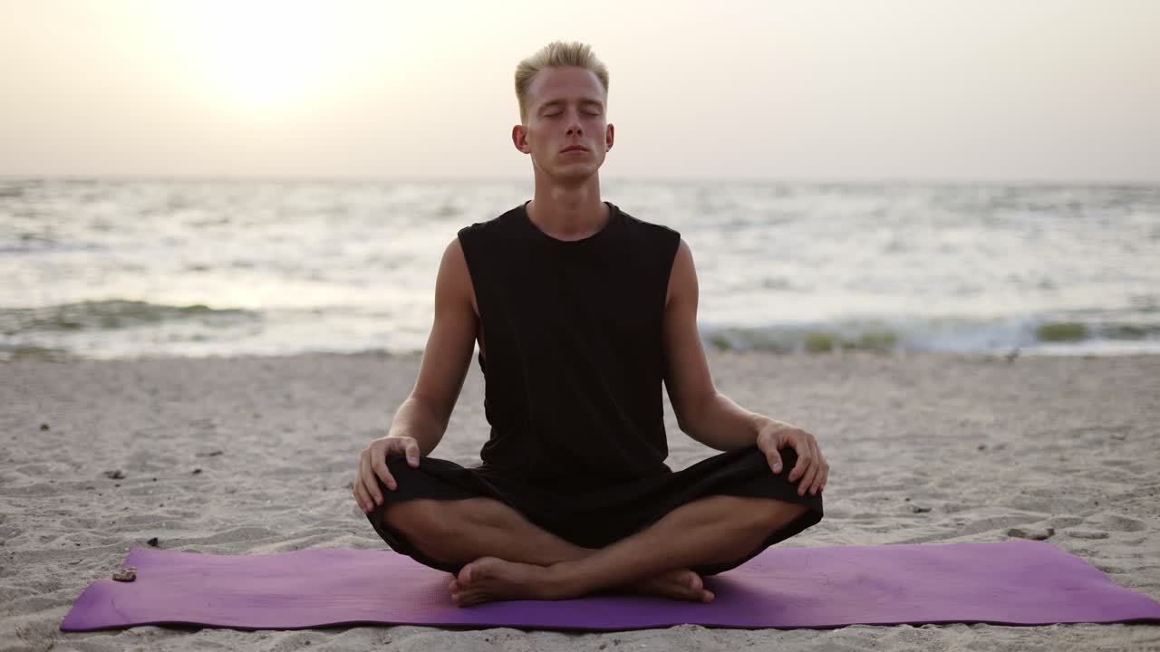 A young man is doing yoga and meditating on a sports mat while sitting during the dawn of the sun. Doing a specific exercise. Meditation, hands. Leisure time, recreation