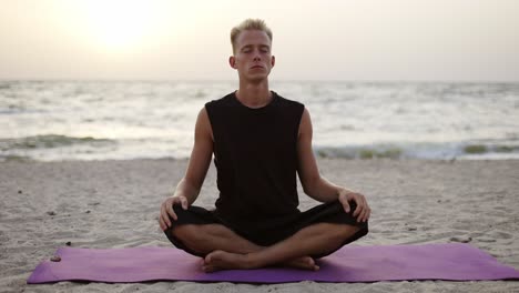 Un-Joven-Está-Haciendo-Yoga-Y-Meditando-En-Una-Alfombra-Deportiva-Mientras-Se-Sienta-Al-Amanecer-Del-Sol.-Haciendo-Un-Ejercicio-Específico.-Meditación,-Manos.-Tiempo-Libre,-Recreación