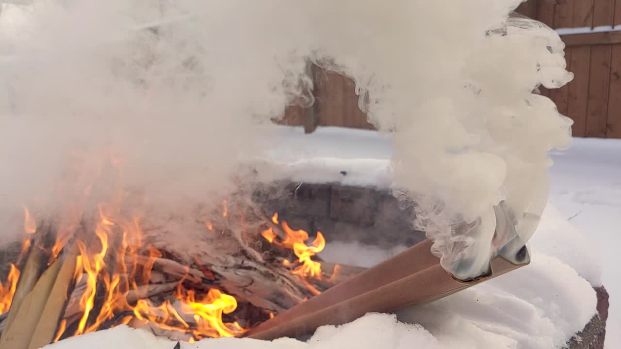 짙은 흰색 - 회색 연기가 카드 보드 튜브에서 솟아오르고 뒷면에서 타오르는 불이 으르렁거립니다.