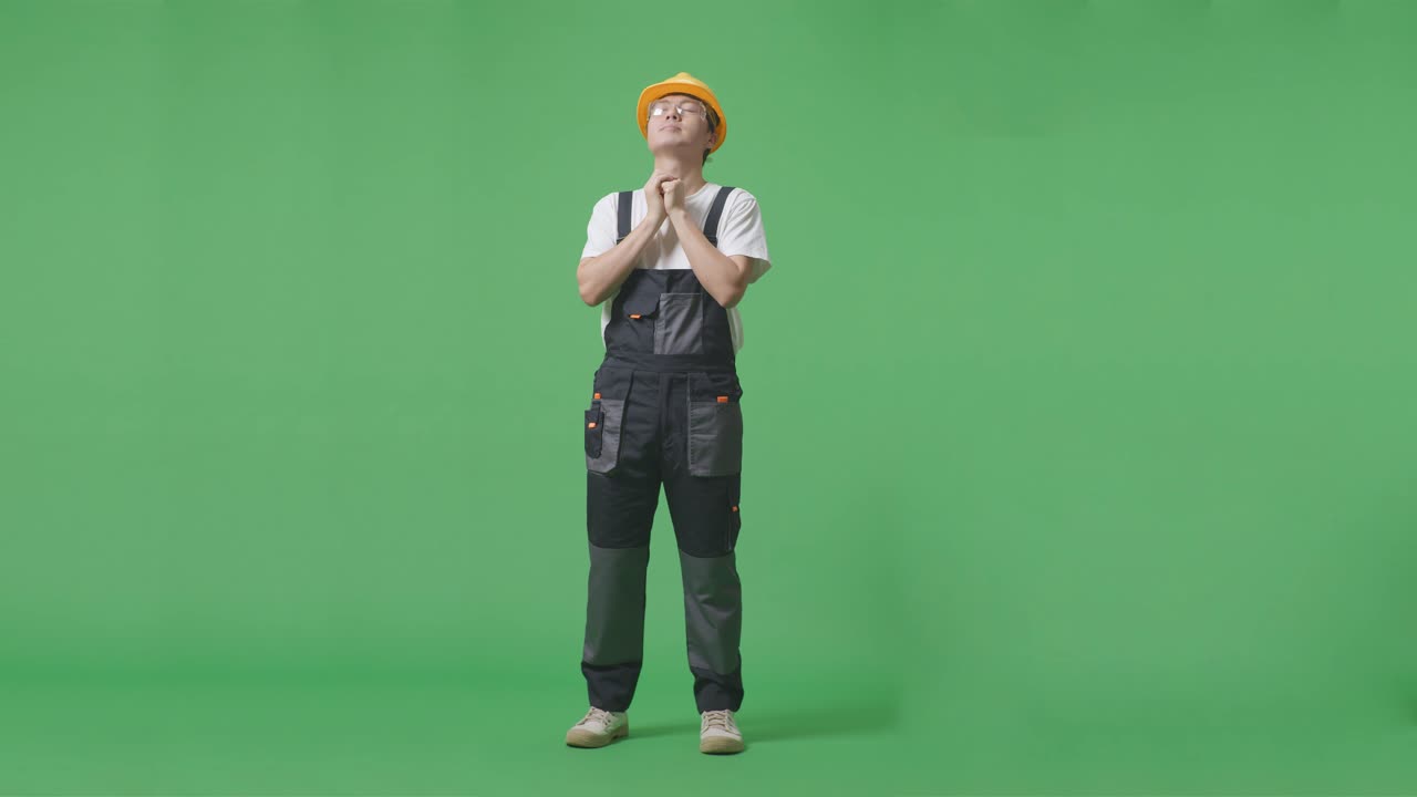 cuerpo lleno de hombre asiático trabajador con gafas de protección y casco de seguridad orando por algo mientras estaba de pie en la pantalla verde estudio de fondo