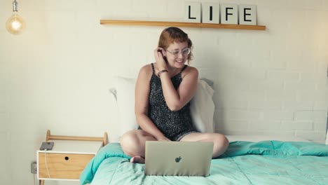 young woman makes a video call on laptop, interacts smiles sitting on bed in bright bedroom