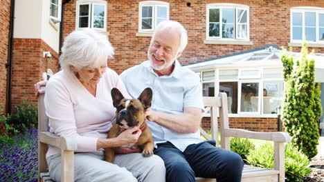 Retired-Couple-Sitting-On-Bench-And-With-Pet-French-Bulldog-In-Assisted-Living-Facility