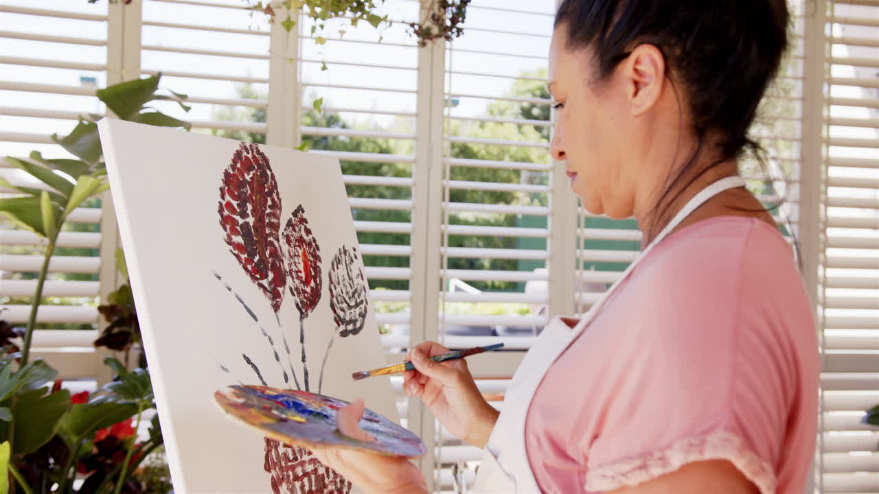 Painting on canvas, woman creating floral artwork with brush and palette