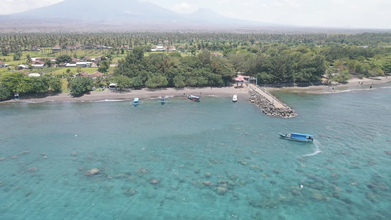 4K drone footage captures a pristine beach with soft white sand and clear turquoise waters, where boats sail by, creating a perfect tropical getaway for tourists seeking relaxation and adventure.