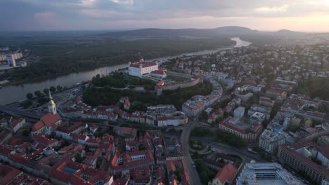toma aérea en órbita del castillo de bratislava o del casco antiguo de bratislavsky hrad al atardecer, el río danubio ondeando hacia las montañas