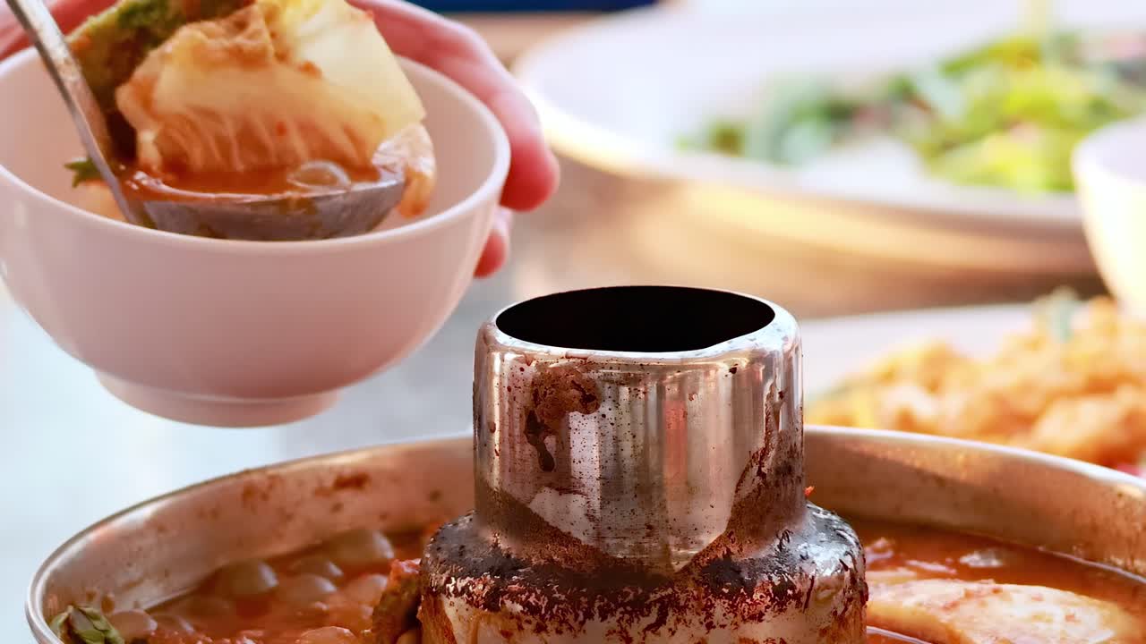 A ladle serves hot soup with vegetables from a metal pot into a bowl.