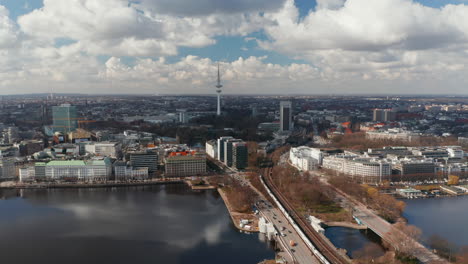 Aerial-view-of-traffic-across-Binnenalster-lake-with-Hamburg-panorama-and-TV-tower-in-the-background