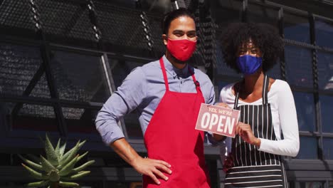 Diverse-cafe-workers-wearing-face-masks-showing-were-open-signage
